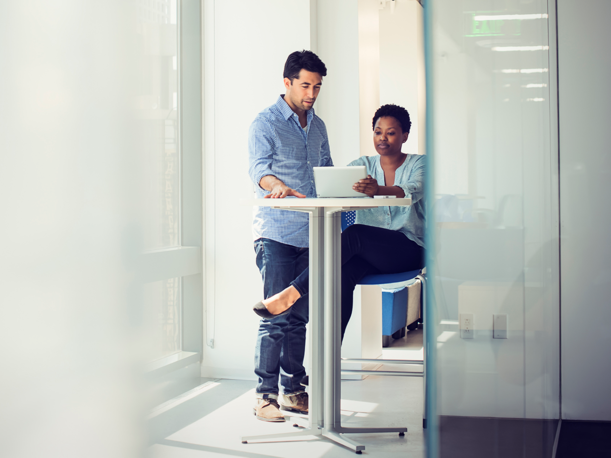 View through an office door of two colleagues chatting at a desk