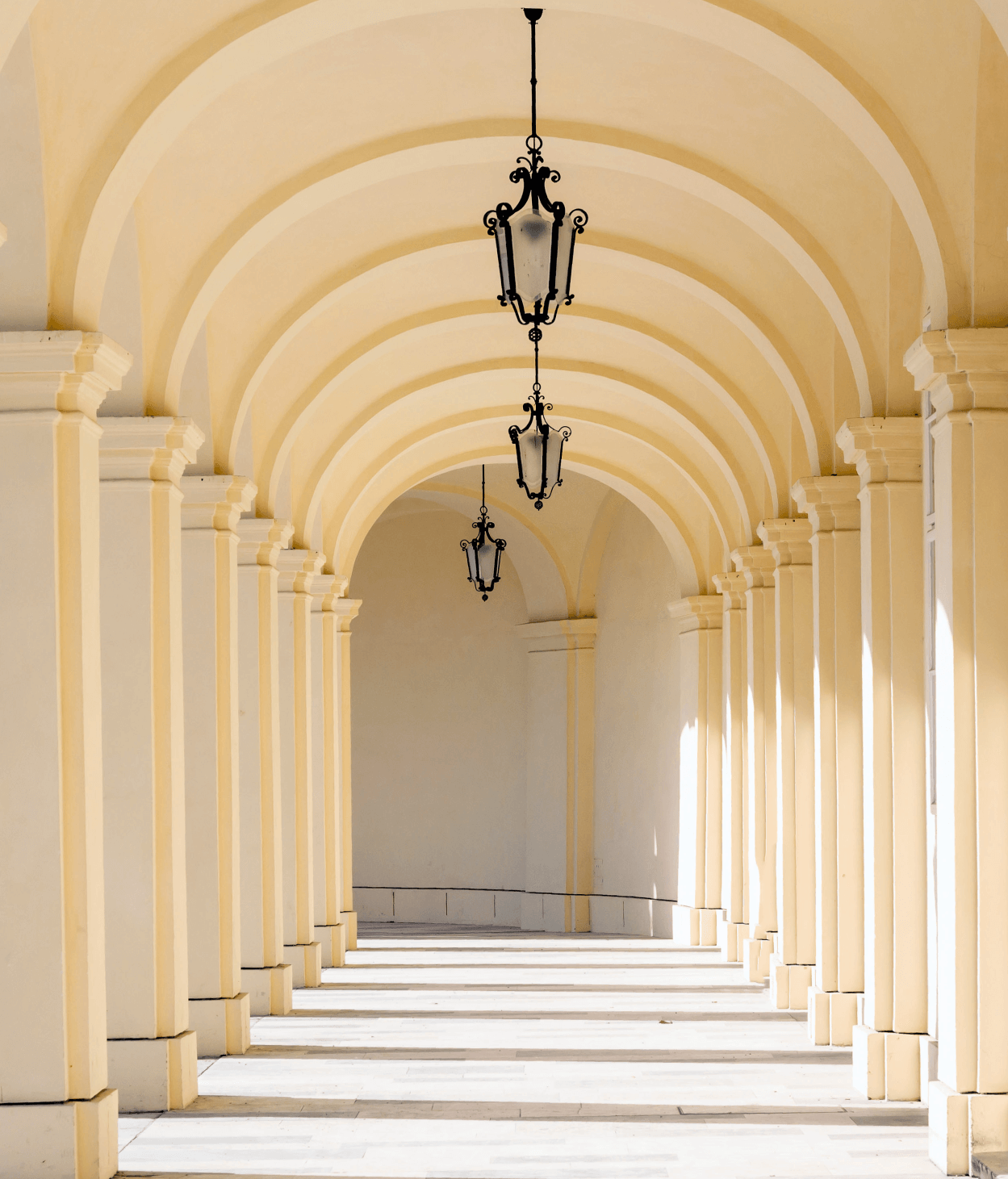 photo of a white arched hallway with lanterns suspended from the ceilings.