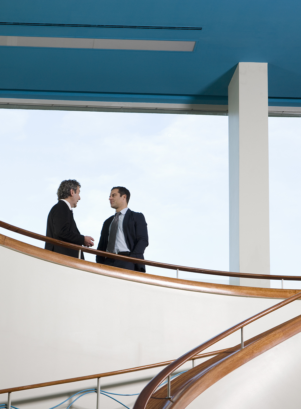 Two businessman hold a conversation on a balcony.